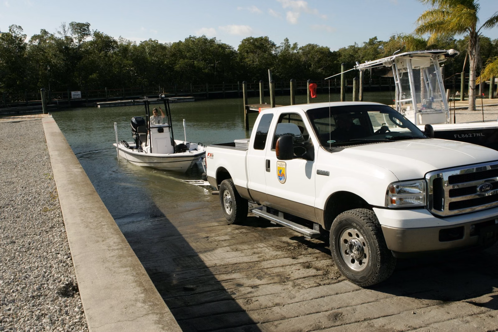 Wildlife workers backing a small boat on a trailer down a ramp into a lake